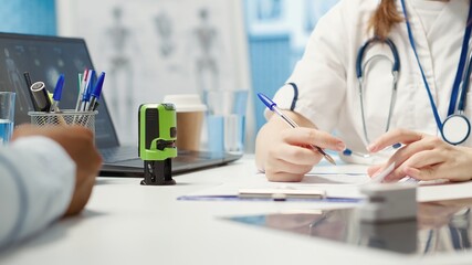 General practitioner putting his stamp on a prescription document for his patient, recommending antibiotics and vitamins as medical treatment. Doctor prescribing medicaments in cabinet. Camera A.