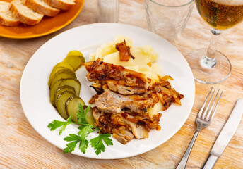 Roasted pork chop with mushed potato and slices of cucumber pickles. Hearty meat dish, hearty snack with alcoholic drink, complemented with pieces of fresh soft baguette.