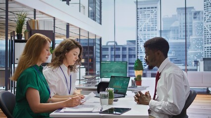 Applicant gives his CV to human resources staff to begin the job interview, reviewing the qualifications and work experience from the application form. Discussing job roles available. Camera B.