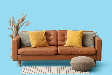 Comfortable sofa with cushions, pouf and pampas grass on blue background
