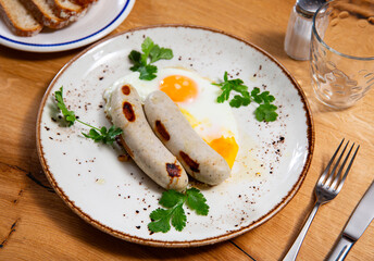 There is freshly cooked breakfast on plate - scrambled eggs with whole of fried pork chicken sausage. Traditional European Spanish breakfast is fried eggs with sausage