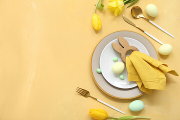 Beautiful table setting with Easter eggs and yellow tulip flowers on color background
