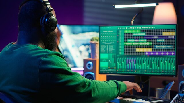 Audio engineer working in home studio with digital software on pc, playing piano keys and editing audio recordings. Musician producer creating tracks on midi controller keyboard notes. Camera A.