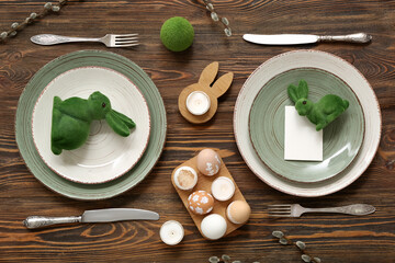 Beautiful table setting with Easter eggs, toy bunnies, burning candles and pussy willow branches on wooden background