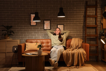 Young woman sitting on sofa in living room at night