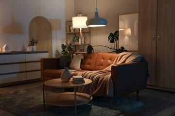 Interior of modern living room with sofa, coffee table and glowing lamps at night