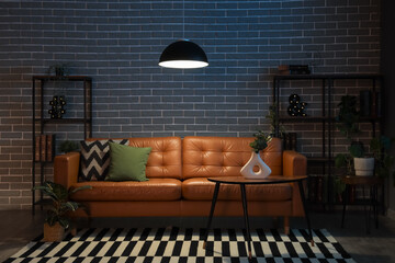 Cozy sofa, coffee table and glowing lamps in interior of stylish living room in evening