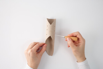 Pair of hands crafting with cardboard tube, punching small holes using a pointed metal tool awl....