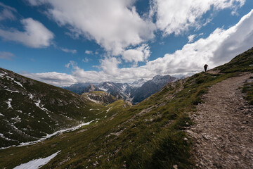 Hiker on a scenic mountain trail with panoramic views of the Dolomites under a dramatic sky.