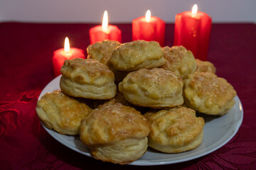 Homemade golden brown cheese scones on a plate with a burgundy tablecloth, surrounded by burning red candles.