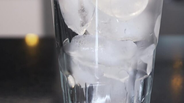 Tilt up a vaso transparente con hielo en una cocina sobre un mes&oacute;n negro.