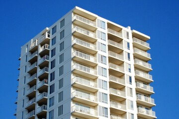 Fototapeta premium A white, modern high-rise building with balconies, against a clear blue sky in the background, in a close-up shot Generative AI
