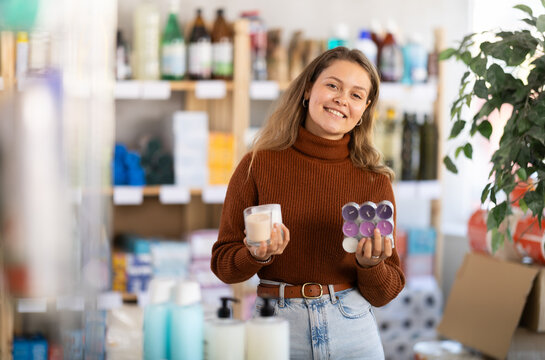 Young woman buyer chooses scented candles in household chemicals store
