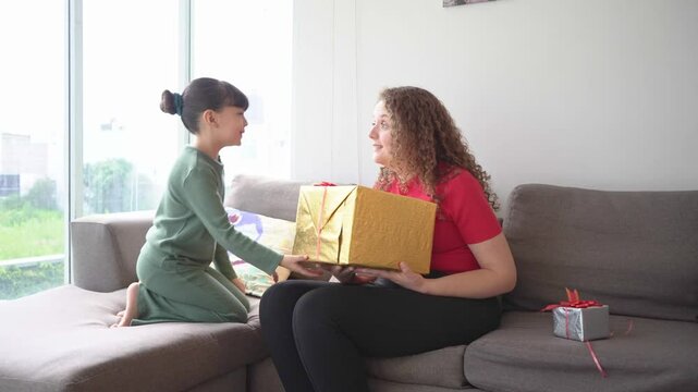 little girl goving a goft box to her mother, mom receiving a present form her child on mother's day