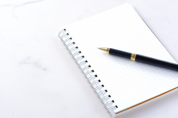 リング式のメモ帳とペンでデスクワークをしているイメージ
