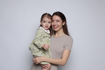 Portrait of happy mother with her cute little daughter on grey background