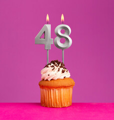 Birthday candle number 48 with cupcake on violet background.