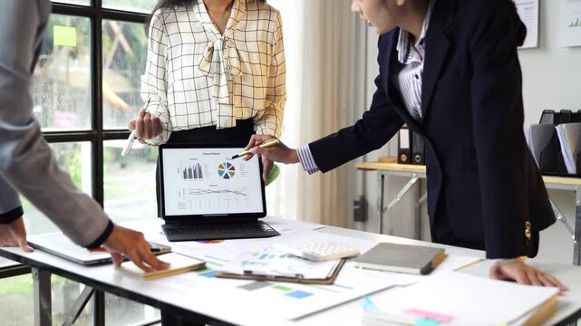 Financial analysis unfolding between two professional businesswomen collaborating over laptop, pointing at marketing strategy charts within bright modern office workspace