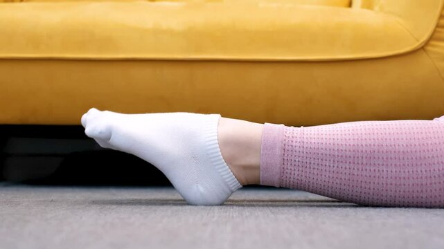 Female legs in socks bend and unbend feet against the background of yellow sofa.