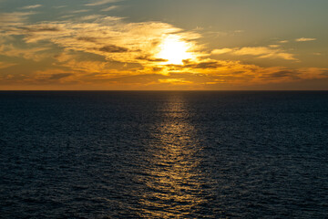 The sun sets on the horizon over the ocean, with colorful and cloudy skies along the coast of Baja California, Mexico.