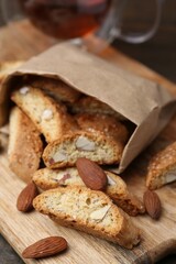 Paper bag with tasty almond biscuits (Cantuccini) and nuts on wooden board, closeup