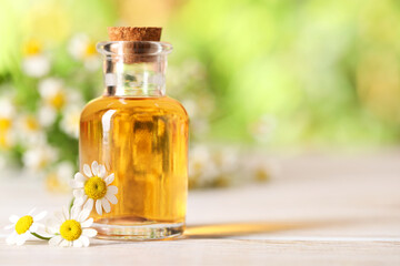 Bottle of essential oil and chamomile flowers on white wooden table against blurred background, closeup. Space for text