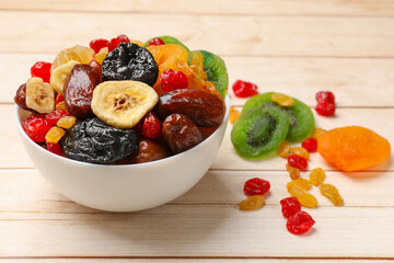 Mix of different dried fruits in bowl on white wooden table, closeup