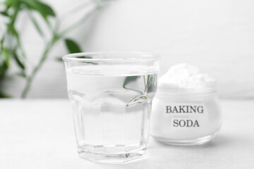 Glass of water and baking soda on white table, selective focus