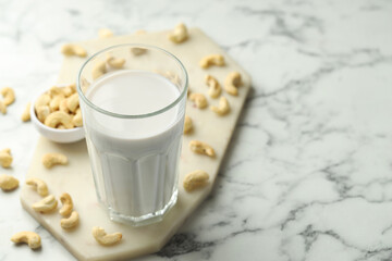 Fresh cashew milk in glass and nuts on white marble table, closeup. Space for text