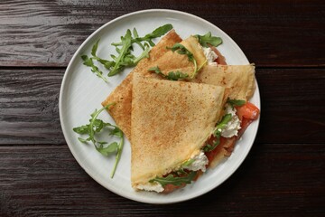 Delicious crepes with salmon, cream cheese and arugula on wooden table, top view