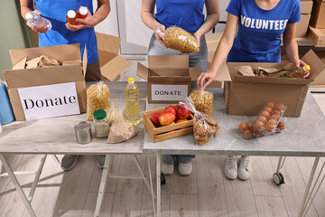 Volunteers packing food donations at tables indoors, closeup