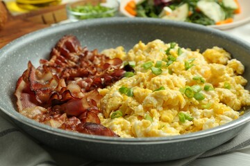 Tasty brunch. Delicious scrambled eggs with bacon and green onions served on white wooden table, closeup