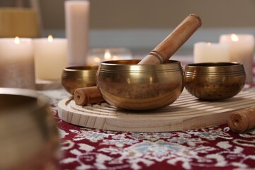 Singing bowls with mallet and burning candles on floor indoors, closeup