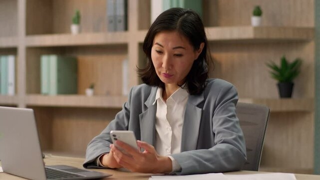 Serious unhappy woman Asian female girl business lady employer chinese korean japanese businesswoman work in office mobile phone browsing search data internet smartphone gadget addicted typing message