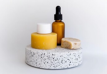 Close up of amber glass bottle, yellow candle, and bar of soap on speckled terrazzo display. Clean, minimalist aesthetic