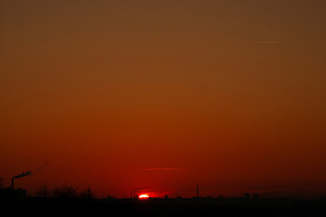 Vivid red sunset nearing horizon over industrial skyline smoke