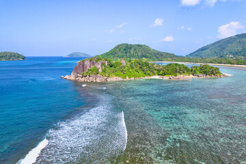 Drone shot of port glaud beach, island in the foreground, coral reef barrier, granite stones, white sandy beach and clear turquoise water, Mahe, Seychelles. 1