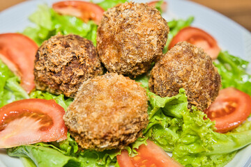 Fried meatballs with cheese fillings, on a bed of lettuce and tomamto salad