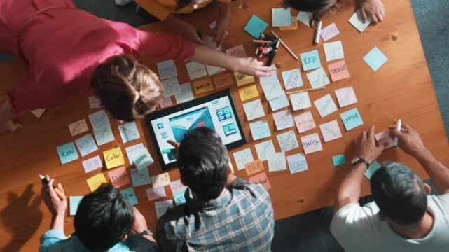 Top down view of programmer brainstorming and planning about web design while looking at tablet wireframe prototype. Aerial view of skilled developer team talking about digital application. Symposium.