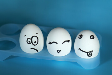 Three white eggs with funny emoji drawn on a blue background. Copyspace