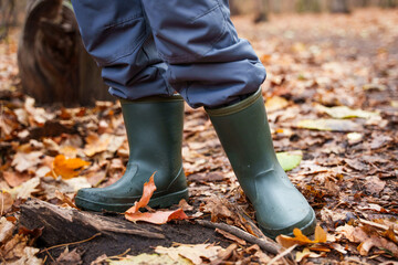 dark green khaki rubber boots on a child in a dirty autumn forest leaves underfoot
