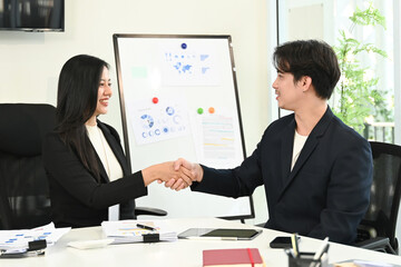 A man shakes hands with a woman in a business meeting.