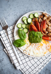 A full protein breakfast with vegetables and mushrooms on a plate. Fried eggs, champignons, tomatoes and green sauce.