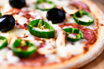 Pizza with salami and mozzarella cheese, jalapeno pepper and black olives. Wooden background. Soft focus. Close up.