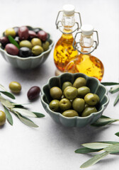 Bowls of green and black olives with olive oil bottles and olive branches on marble table