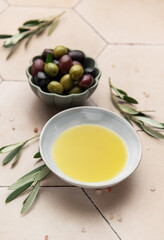Olive oil and olives with olive branches resting on a tiled surface