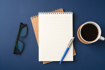 Top view of a workspace with a blank notebook, pen, glasses, coffee