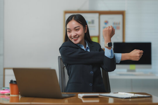 Asian businesswoman stretching arms at office desk with laptop - Powered by Adobe