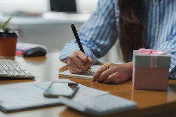 Fototapeta premium Office worker writing a greeting card next to a gift