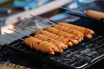 Close-up photo of some sausages being grilled, the handles of the sausages are made of bamboo skewers